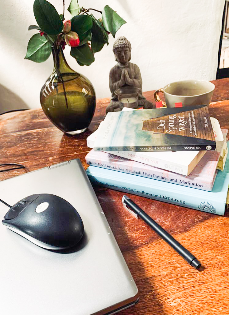 Tisch mit Büchern, PC, Stiften, Blumen und Buddha Figur